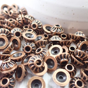 May include: A large pile of antique copper-toned metal beads with a decorative design. The beads have a small hole in the center for stringing.