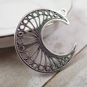 May include: Silver filigree crescent moon charm with a delicate, intricate design. The charm has a loop at the top for attaching to jewelry or other crafts.