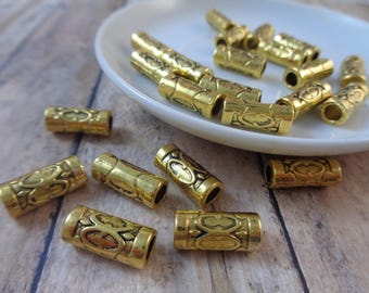 May include: A collection of gold-toned metal beads with an intricate design. The beads are cylindrical and have a textured surface.