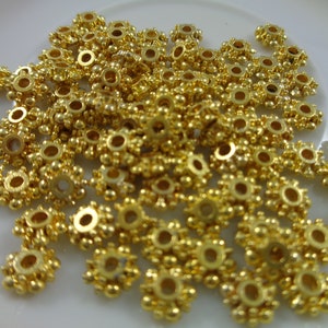 May include: A pile of gold-colored metal beads with a starburst design. The beads have a small hole in the center for stringing.