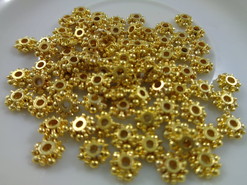 May include: A pile of gold-colored metal beads with a starburst design. The beads have a small hole in the center for stringing.