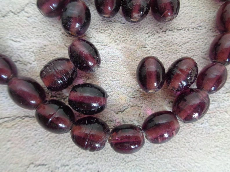 May include: A strand of deep purple glass beads, each bead is oval shaped and has a slight iridescent sheen.