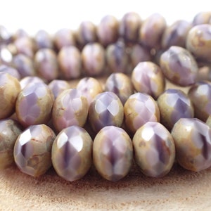 May include: A strand of faceted glass beads with a purple and brown marbled pattern. The beads are oval shaped and have a glossy finish.