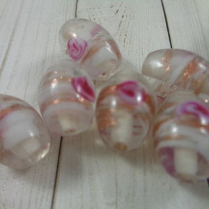 May include: Six white glass beads with pink and gold swirls. The beads are oval shaped and have a hole through the center.