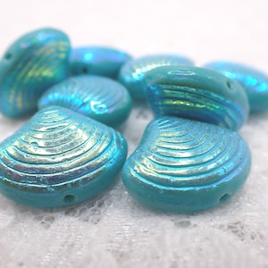 May include: A collection of iridescent turquoise seashell-shaped beads. The beads have a glossy finish and are designed with detailed ridges. These beads are ideal for jewelry making and crafting projects.