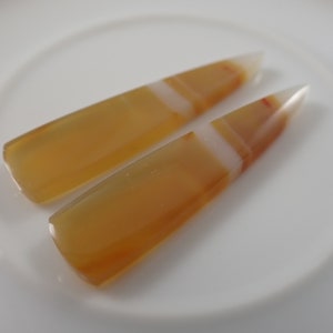 May include: Two agate points with a white and orange banded pattern. The points are on a white surface.