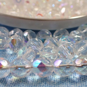 May include: A strand of iridescent clear glass beads with faceted edges. The beads are strung on a silver wire and have a rainbow sheen.