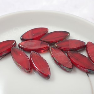 May include: A group of red glass beads in an oval shape. The beads have a striated pattern and a glossy finish.