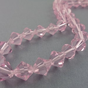 Puede incluir: Una hebra de cuentas de cristal facetadas de color rosa. Las cuentas est&aacute;n enhebradas en un hilo transparente y est&aacute;n dispuestas en un patr&oacute;n repetitivo.