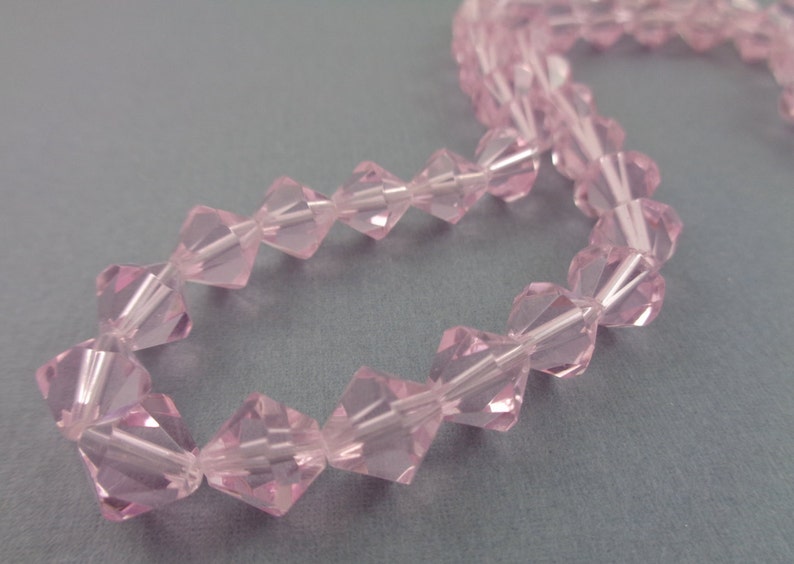 Puede incluir: Una hebra de cuentas de cristal facetadas de color rosa. Las cuentas est&aacute;n enhebradas en un hilo transparente y est&aacute;n dispuestas en un patr&oacute;n repetitivo.