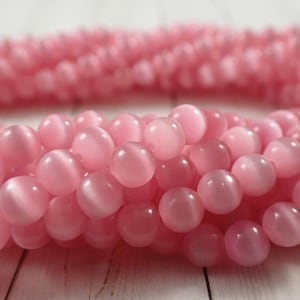 May include: A strand of pink cat's eye beads. The beads are round and have a smooth, shiny finish.