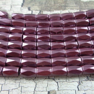 May include: A strand of dark purple faceted glass beads. The beads are rectangular in shape and have a glossy finish.