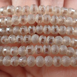 May include: A strand of translucent, frosted glass beads with a silver iridescent sheen. The beads are round and have a textured surface.