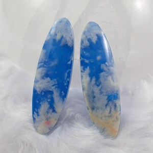 May include: Two oval-shaped cabochons with a blue and white cloudy pattern. The cabochons are translucent and have a slight shimmer.