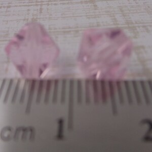 Puede incluir: Dos cuentas de cristal facetadas de color rosa, cada una mide aproximadamente 1 cm de di&aacute;metro, se muestran junto a una regla.