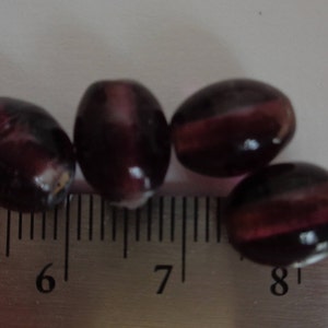 May include: Four purple glass beads with a striated pattern, measured on a ruler with markings from 5 to 9 inches.