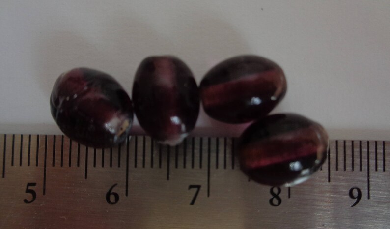 May include: Four purple glass beads with a striated pattern, measured on a ruler with markings from 5 to 9 inches.