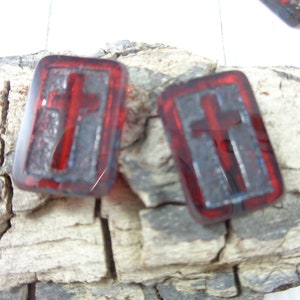 May include: Two red glass tiles with a silver cross design. The tiles are rectangular and have a slightly textured surface.
