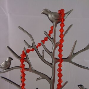 May include: A silver metal jewellery tree with three bird perches and a red crystal necklace draped over the branches.