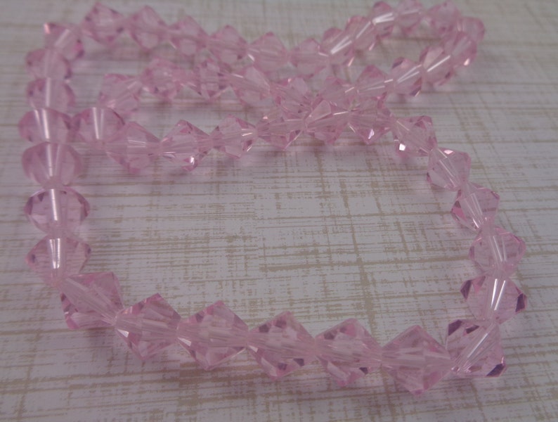 Puede incluir: Una hebra de cuentas de cristal rosa. Las cuentas son facetadas y tienen forma de diamante.