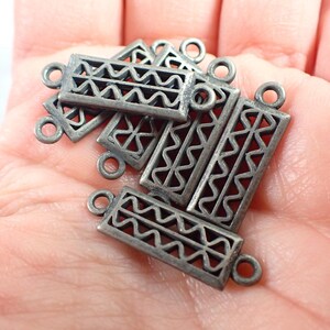 May include: A collection of antique silver-colored rectangular jewelry clasps. Each clasp features a decorative openwork design with a zigzag pattern and small loops on each end for attachment. The clasps are shown in a person's hand.