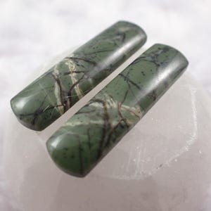 May include: Two green and white marbled cabochons with a rectangular shape. The cabochons have a smooth, polished surface.