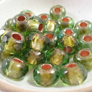 May include: A group of green glass beads with gold accents. The beads have a faceted design and a hole in the center for stringing.