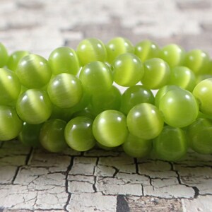 May include: A strand of green cat's eye beads. The beads are round and have a smooth, polished finish. They are strung on a clear elastic cord.
