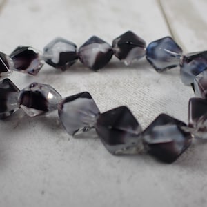 May include: A strand of faceted beads with a mix of black, white, and clear colors. The beads have a geometric shape and are strung together, creating a decorative element.
