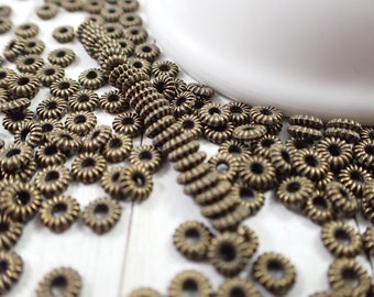 May include: A close-up of a pile of antique gold-toned metal beads. The beads are round and have a decorative, raised design.