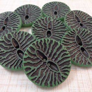 May include: A collection of eight round buttons with a unique design. The buttons feature a green outer rim and a black, textured center with a central oval hole and two smaller holes. The buttons are likely for sewing or crafts.