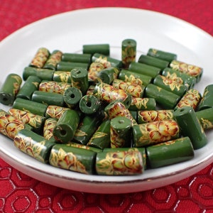 May include: A bowl of green wooden beads with gold and orange floral designs. The beads are cylindrical and have a smooth finish.