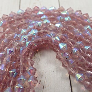 May include: A strand of iridescent pink glass beads with a faceted, star-shaped design. The beads are strung on a clear thread and have a subtle shimmer.