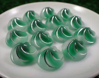 May include: A collection of 13 green and silver swirl-shaped buttons on a white plate.