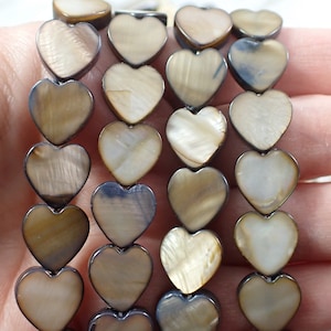 May include: A strand of brown and white heart-shaped shell beads. The beads have a natural, iridescent finish.
