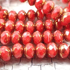 May include: Close-up of a strand of red faceted glass beads with a gold metallic finish. The beads are round and have a slightly irregular shape.
