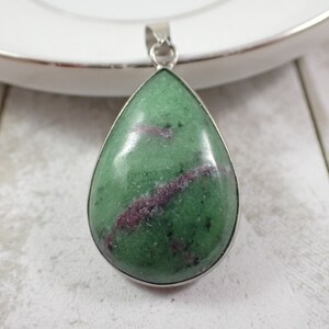 May include: A teardrop-shaped pendant with a green and purple gemstone set in a silver setting.