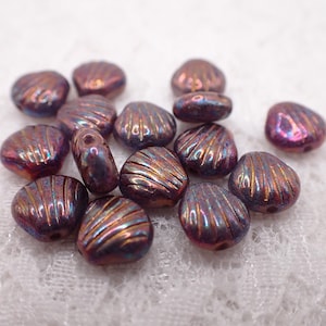 May include: A collection of iridescent, shell-shaped beads. The beads are primarily purple with gold and blue highlights, and feature a ridged texture. These decorative beads are suitable for jewelry making and craft projects.