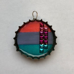 May include: A bottle cap pendant with a layered design of coral, purple, and teal colours. A vertical line of pink and blue iridescent squares is centred on the cap.