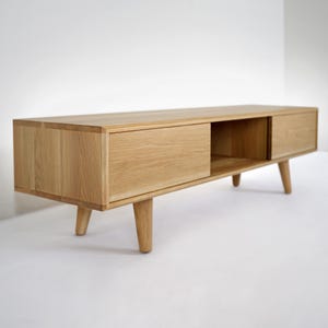 May include: A light wood TV stand with two sliding doors and a shelf. The stand has four short, tapered legs.