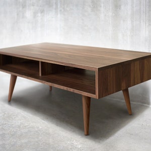 May include: A mid-century modern coffee table made of walnut wood with a rectangular top and two open shelves. The table has four tapered legs.