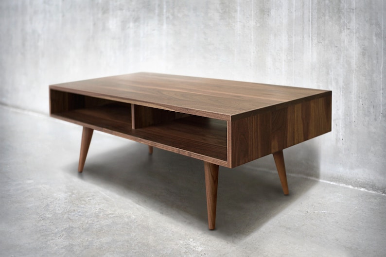 May include: A mid-century modern coffee table made of walnut wood with a rectangular top and two open shelves. The table has four tapered legs.