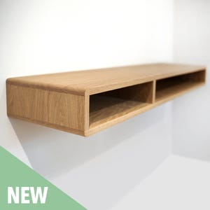 May include: A light wood floating shelf with two open compartments. The shelf is mounted on a white wall.