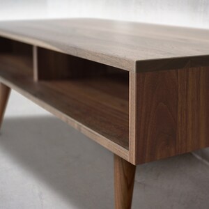 May include: A wooden coffee table with a rectangular top and two open shelves. The table has a dark brown finish and tapered legs.