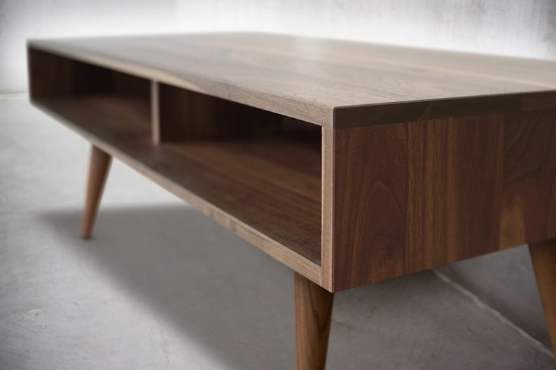 May include: A wooden coffee table with a rectangular top and two open shelves. The table has a dark brown finish and tapered legs.