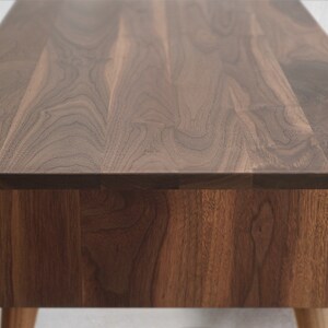 May include: A close-up of a wooden table top with a natural walnut finish. The table has a simple, modern design and is made of high-quality wood.