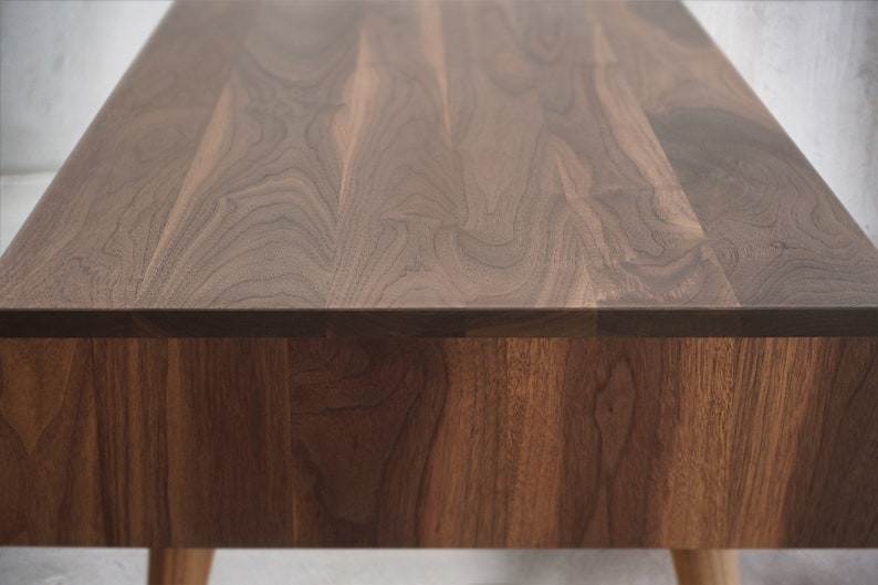 May include: A close-up of a wooden table top with a natural walnut finish. The table has a simple, modern design and is made of high-quality wood.
