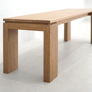 May include: A light wood bench with a rectangular top and four legs. The bench is made of solid wood and has a natural finish.