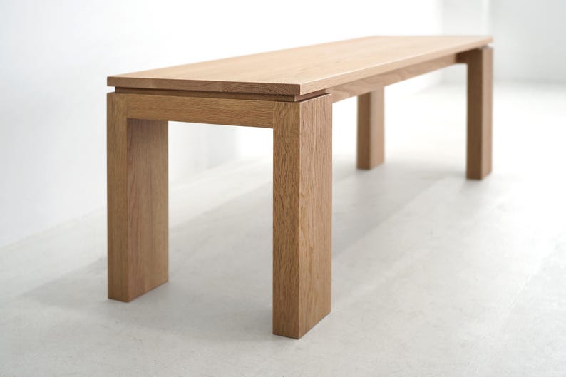 May include: A light wood bench with a rectangular top and four legs. The bench is made of solid wood and has a natural finish.