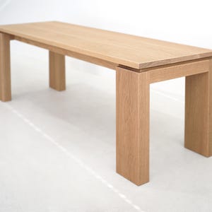 May include: A light wood bench with a rectangular top and four legs. The bench is made of solid wood and has a natural finish.
